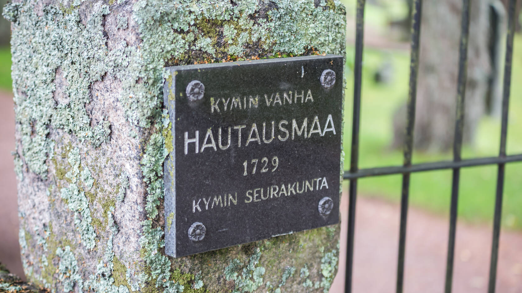 Kivitolpassa hautausmaan nimikyltti ja rauta-aitaa.