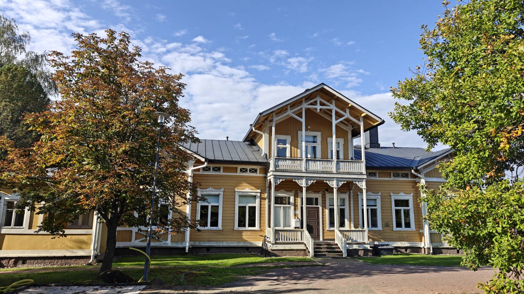 Vanha, koristeellinen puutalo, jonka edessä puita.