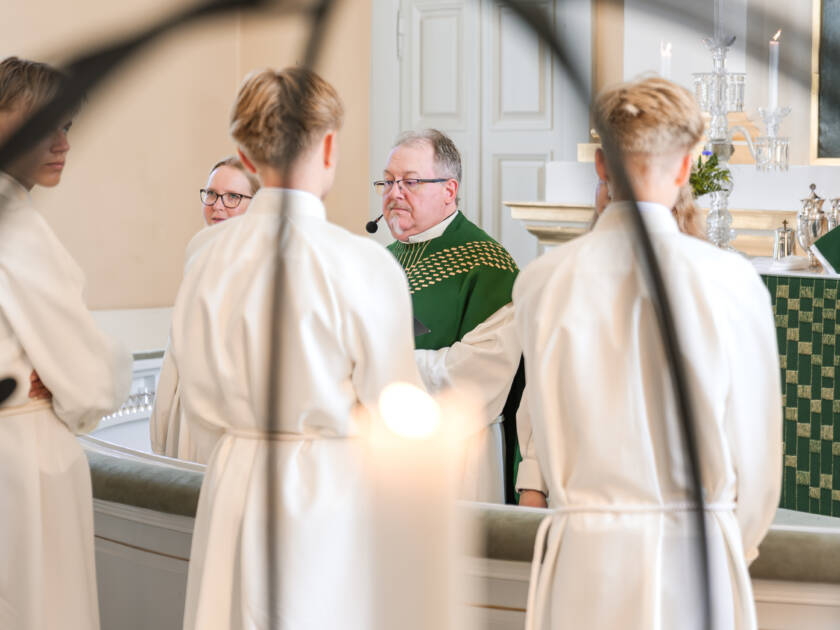 Nuoria kirkon alttarilla, albat päällä, alttarin toisella puolella kaksi työntekijää.