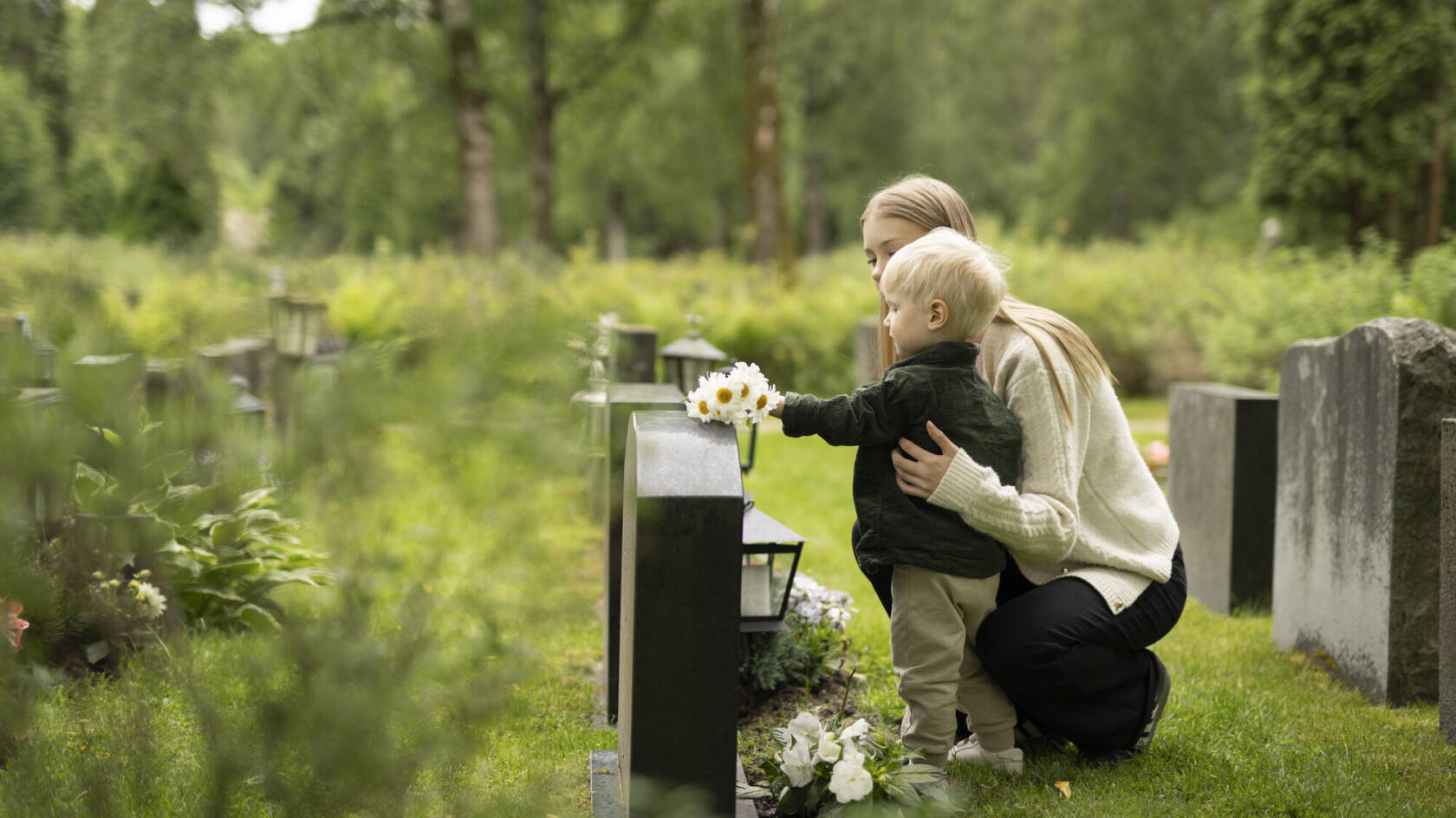 Nainen ja lapsi laittavat kukkia haudalle.